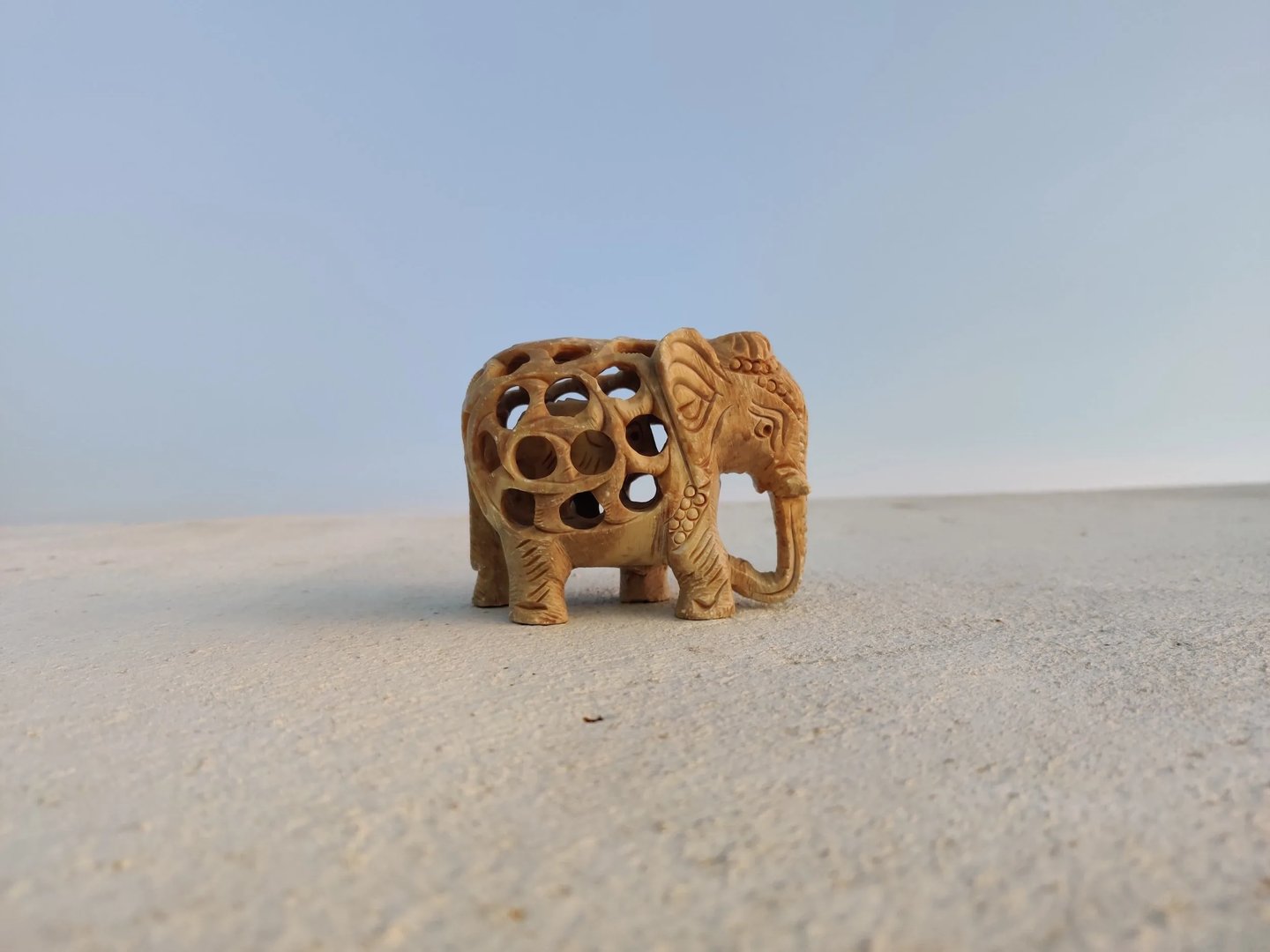 Small hand-carved wooden elephant figurine with an openwork lattice body, standing on sand